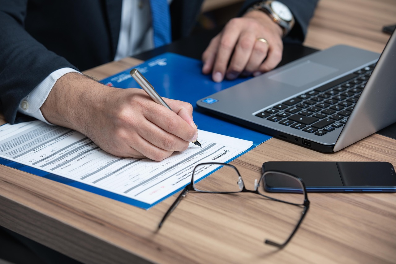 A person signing documents next to a laptop